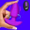 Purple silicone pleasure toy being held by a hand against a vibrant blue background