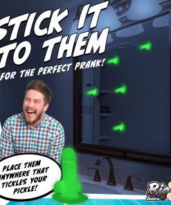 A man laughs in front of a mirror with green prank items displayed.