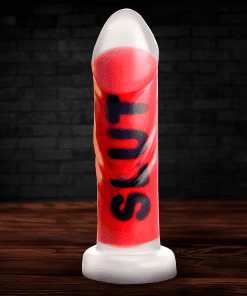 A vibrant red silicone novelty item with the word 'SLUT' printed on it, displayed on a wooden table against a dark brick background.