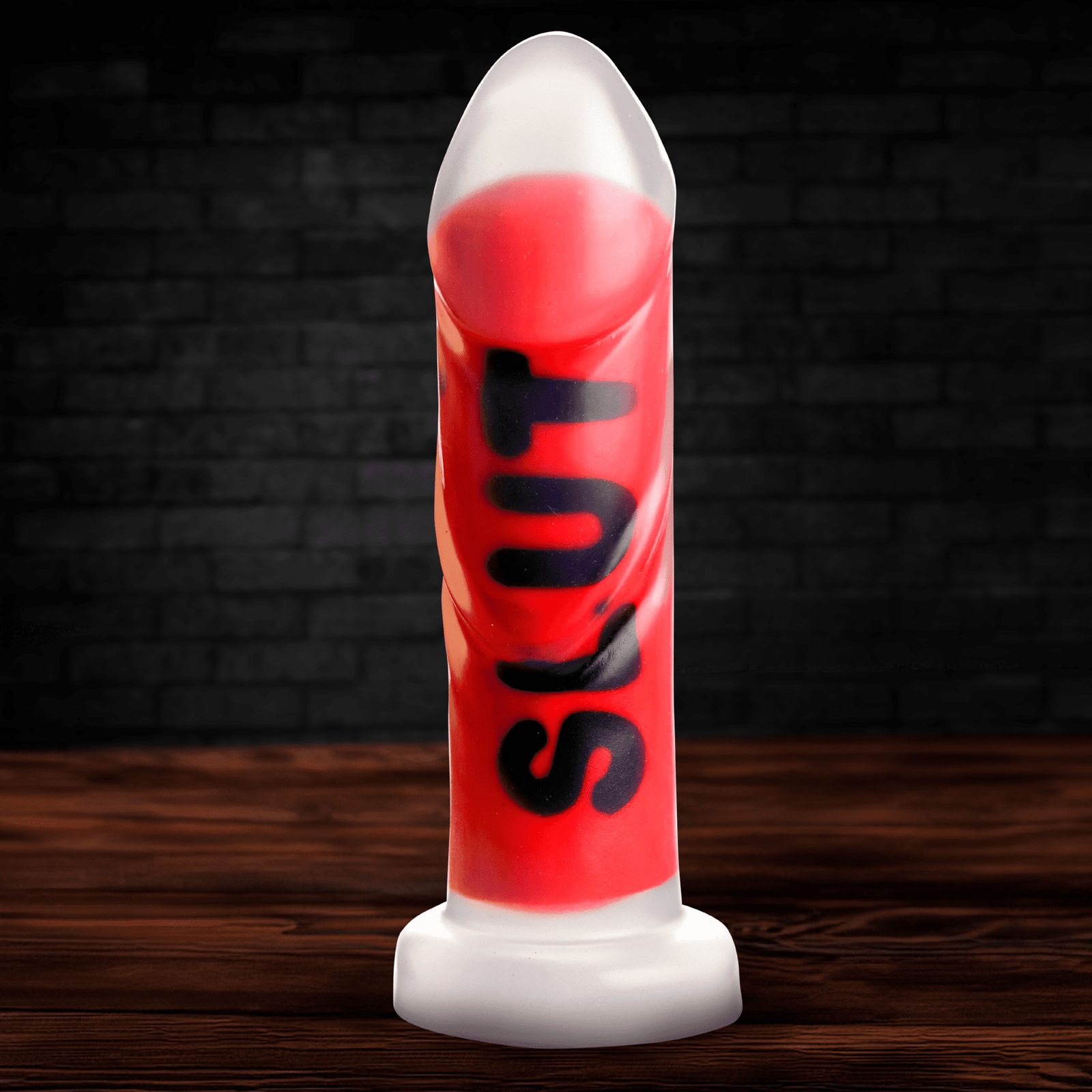 A vibrant red silicone novelty item with the word 'SLUT' printed on it, displayed on a wooden table against a dark brick background.
