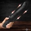 Hand holding a black silicone toy against a dark brick background
