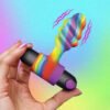 A colorful vibrator held in a hand with a vibrant background